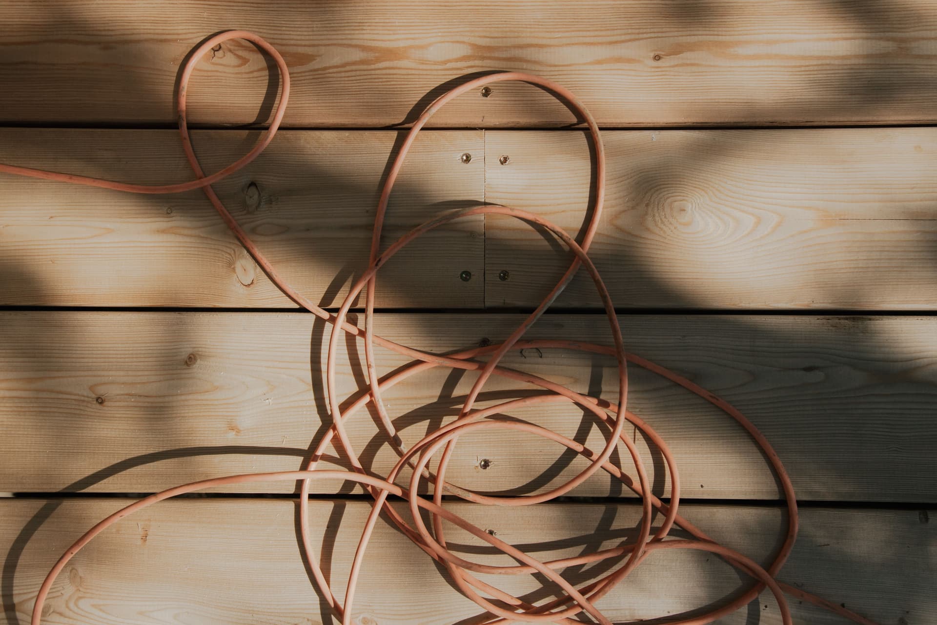 An orange cable lying tangled on a sunlit wooden plank surface